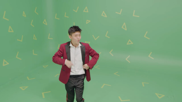 Rich Brian mengenakan jas merah dan hitam sambil berpose di depan green screen dalam MV “Love In My Pocket”